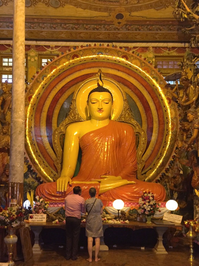 At the Gangaramaya Buddhist Temple, Raschman offers a blessing to Buddha on my behalf, asking for a safe journey for me and MacGyver in Sri Lanka.